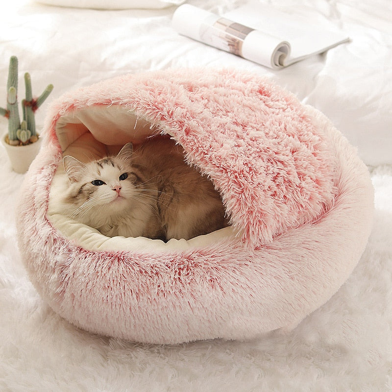 Cat lying in a pink plush pet bed on a white surface with a plant in the background