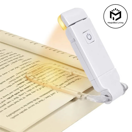 A white pocket book light with a clear clip, shown clipped to an open book. The device has a power button on top and a small warm light glowing at the tip.